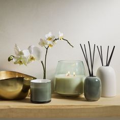 candles and vases on a shelf with orchids in the center, one candle is lit