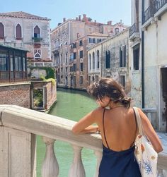 a woman standing on a bridge looking at the water and buildings in venice, italy