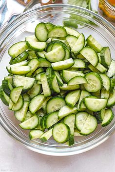 a glass bowl filled with sliced cucumbers on top of a white tablecloth