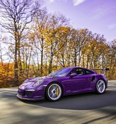 a purple sports car driving down the road with trees in the backgrouund