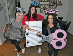 three women dressed up in costumes holding giant scissors and paper cutouts with words on them