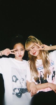 two young women sitting next to each other in front of a black background with one pointing at the camera