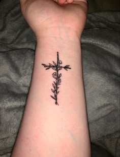 a cross with flowers on the wrist is shown in black ink, while someone's hand holds it up