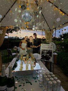 two women and a man are standing under a tent with wine glasses on the table