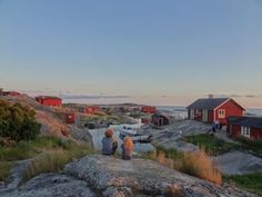 two people are sitting on a rock looking at the water and houses in the distance