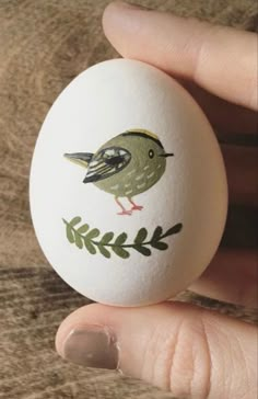 a hand holding an egg with a bird painted on it's side and green leaves