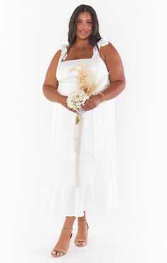 a woman in a white dress is holding a bouquet and posing for the camera with her hands on her hips