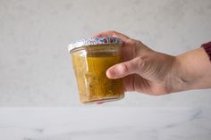 a hand holding a jar of mustard on top of a white counter with a gray wall in the background