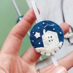 a hand holding a small blue and white brooch with a house on it's side