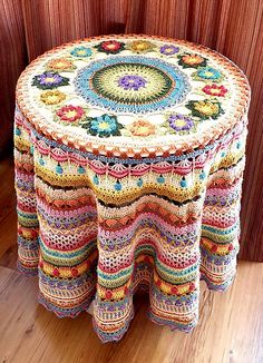 a multicolored crocheted table sits in front of a red curtain and wooden floor