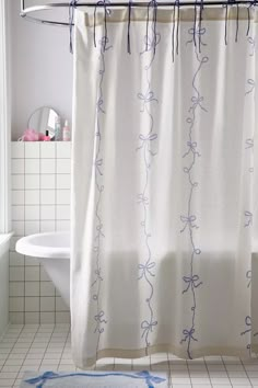 a bathroom with a shower curtain that has blue vines on it, and a bathtub in the background