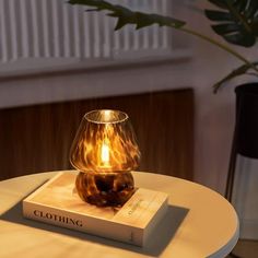 a table with a book on it and a lamp sitting on top of it next to a potted plant