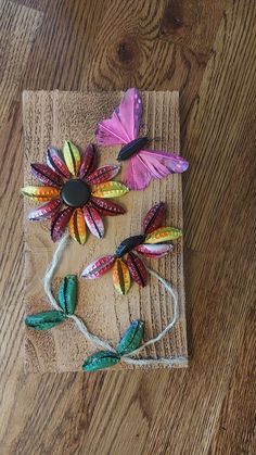 three paper flowers on a piece of wood with string attached to the top and one flower in the middle