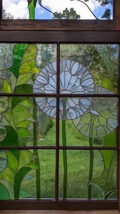 a close up of a stained glass window with grass and trees in the background on a sunny day