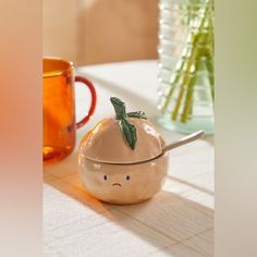 an orange shaped container with a spoon in it sitting on a table next to two vases