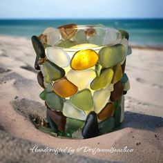 a glass candle holder made out of sea glass on the beach