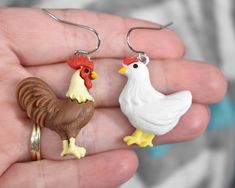 two small chicken earrings are being held in someone's hand while they both have brown and white roosters on them