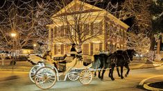 two horses pulling a carriage with people in it down the street at night time,