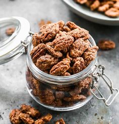 a glass jar filled with nuts on top of a gray counter next to another bowl full of nuts