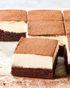 several pieces of cake sitting on top of a white counter next to some brownies