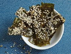 sesame seeds and seaweed in a small white bowl on a blue tableclothed surface