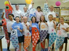 a group of children holding up kites in front of a classroom table with paper lanterns