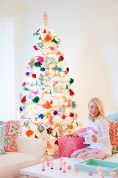 a woman sitting in front of a white christmas tree with pom - poms