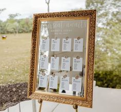 a gold framed mirror with seating cards attached to it and a tree in the background