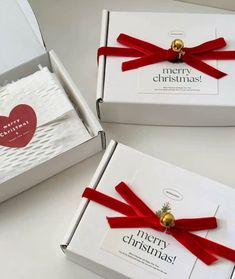 two white boxes with red ribbon and gold bells on them, each containing a christmas card