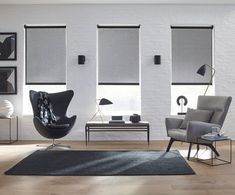 a living room filled with furniture and windows covered in roller shades on white brick walls