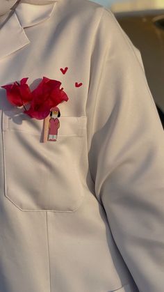 a person wearing a white lab coat with a red flower in the pocket