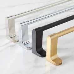 three different colored metal handles on a marble counter top, one black and the other gold