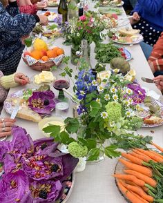 people sitting at a long table with plates of food and vegetables on it, all in front of them