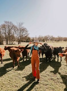 a woman standing in front of a herd of cows on top of a grass covered field