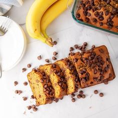 sliced loaf of chocolate chip banana bread next to two bananas on a white counter top