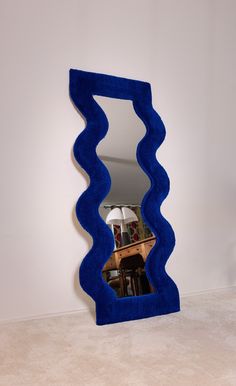 a blue mirror sitting on top of a floor next to a white wall with a reflection in it