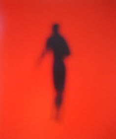 the shadow of a person standing in front of an orange wall with a red background