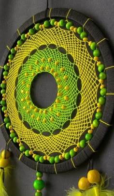 a yellow and green doily is hanging on a gray surface with some beads around it