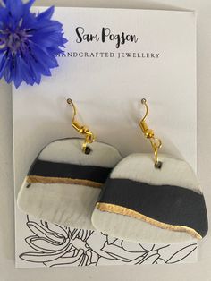 two black and white earrings with gold accents on them next to a blue dandelion