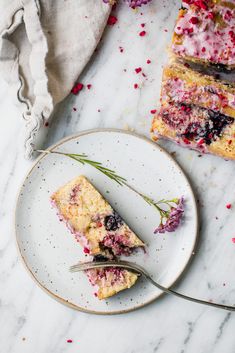 two slices of berry cake on a plate with a fork next to it and another slice in the background