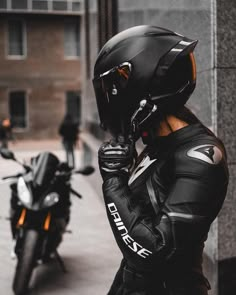 a person wearing a helmet is standing next to a parked motorcycle and talking on the phone