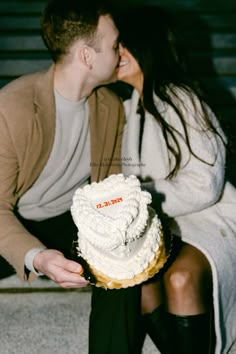 a man and woman kissing while sitting on the ground with a cake in front of them