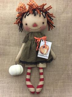 a doll with red hair wearing a green dress and striped socks holding a white pumpkin