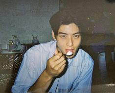 a young man brushing his teeth while sitting at a table