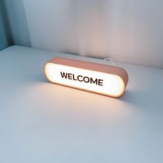 a welcome sign is lit up on a white table top with a blue wall in the background