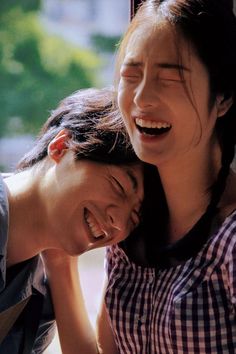 two young women laugh as they sit next to each other in front of a window