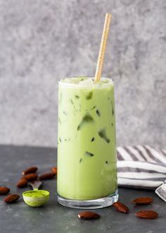 a green smoothie in a glass with a straw and some almonds around it