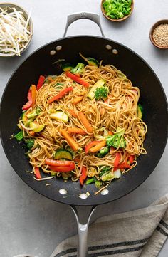 a wok filled with noodles and vegetables on top of a table