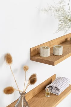 two wooden shelves with candles and towels on them in front of a wall mounted plant