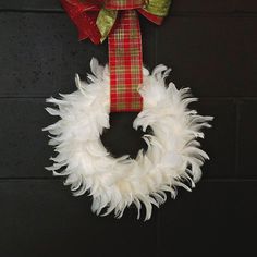 a white wreath hanging on the side of a brick wall with a red and green ribbon